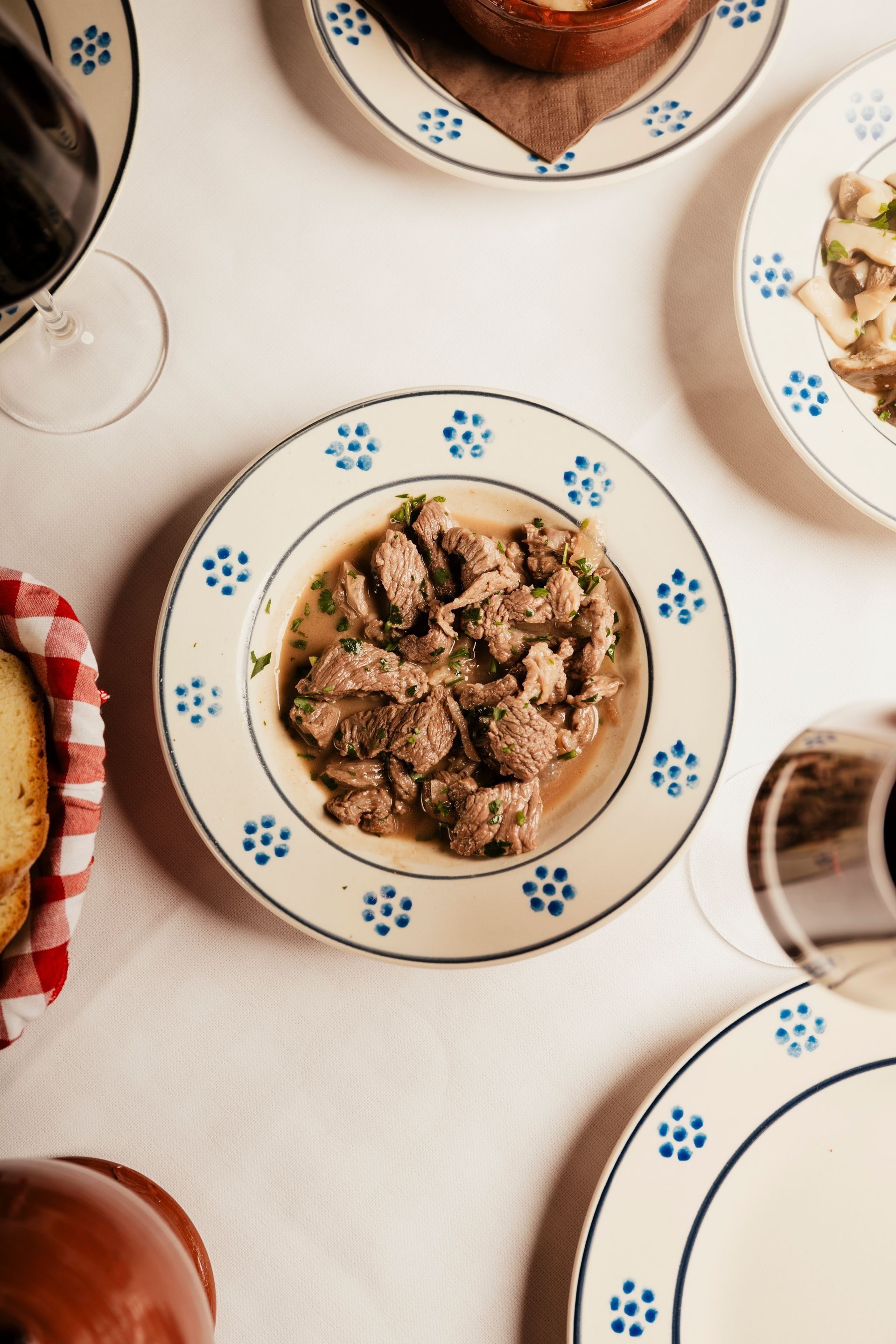 Overhead view of several plates of food on a white table, with wine glasses around them