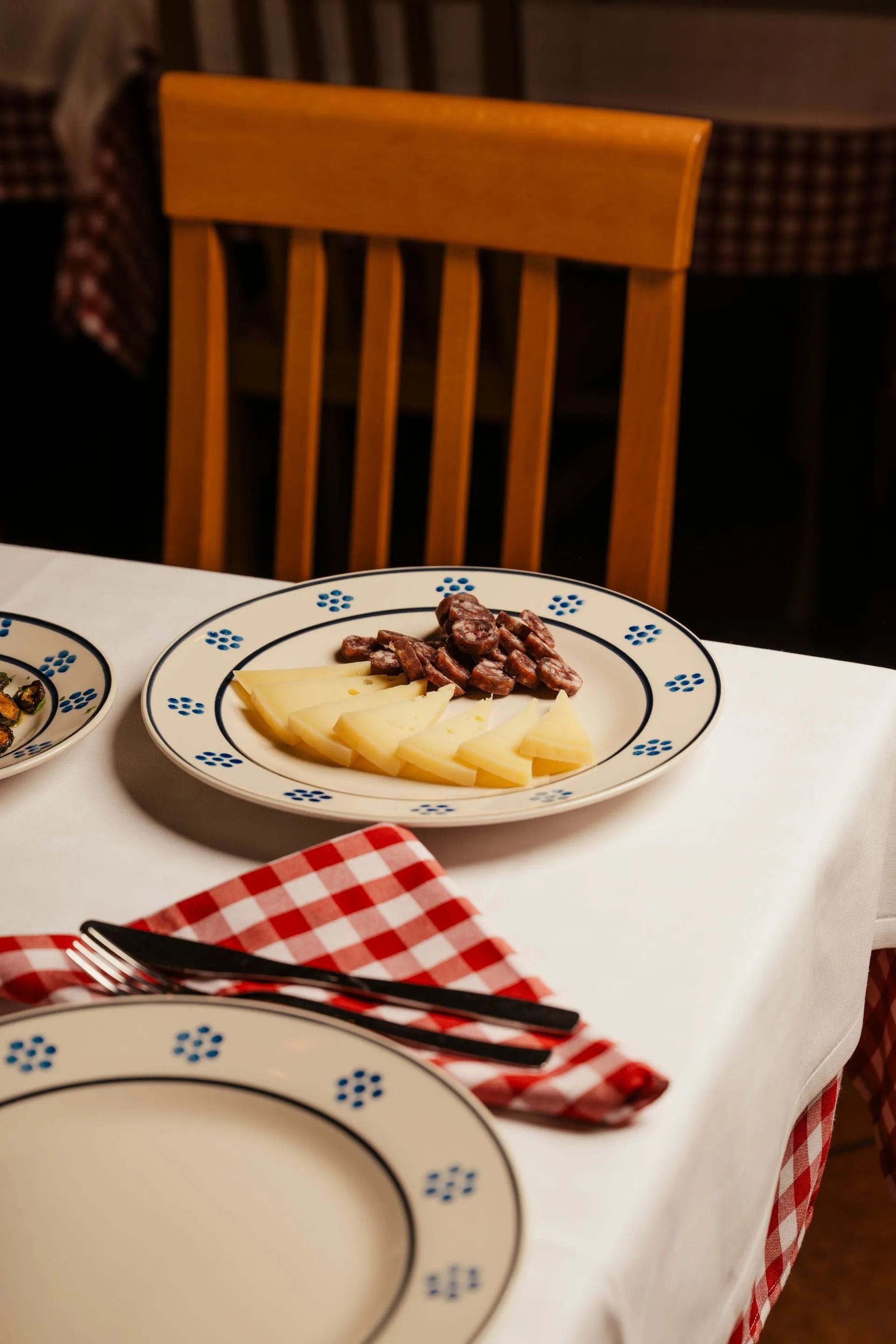 Dining table with plates of food, red checkered napkin, and wooden chair in a cozy restaurant setting