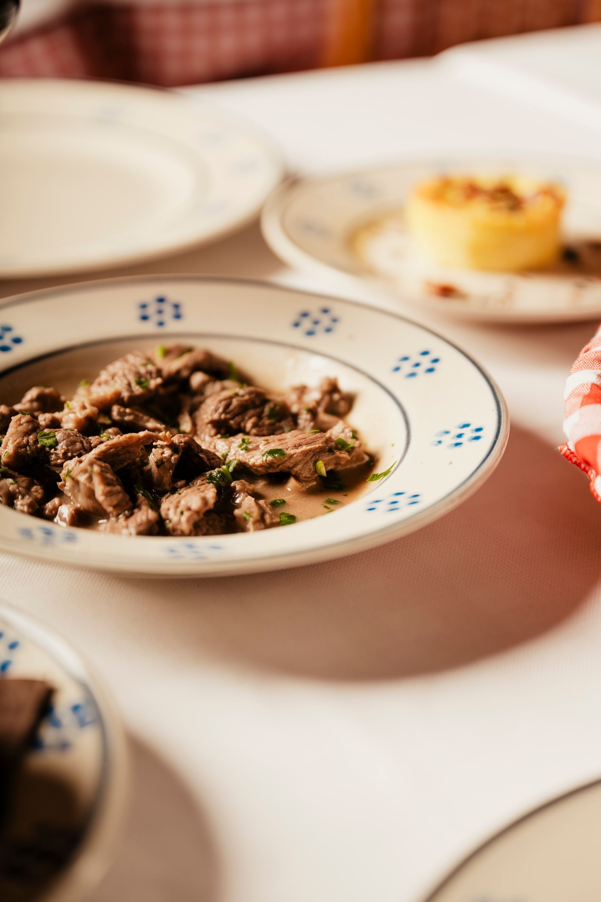 Plated beef dish on a table with a dessert plate in the background