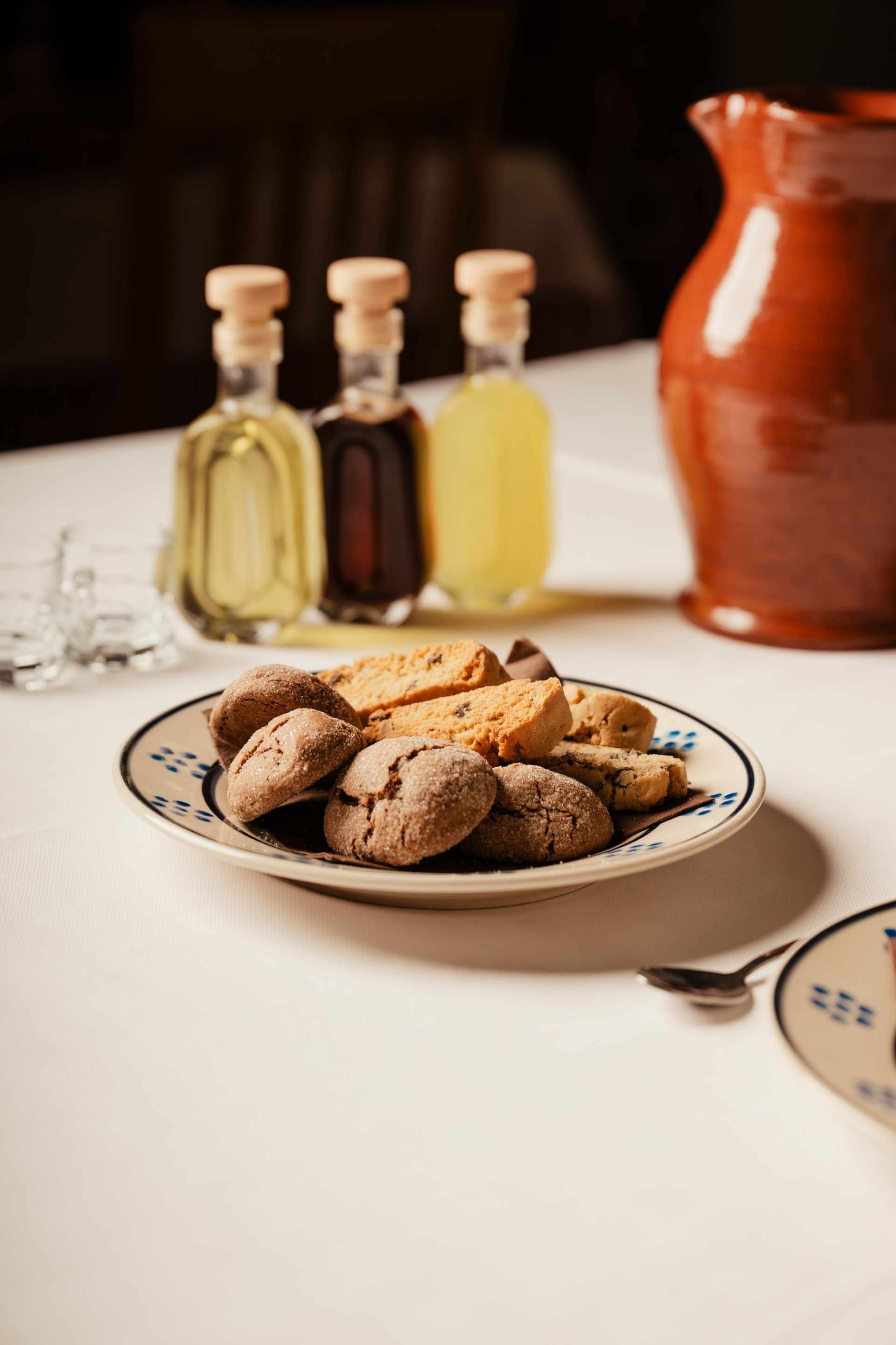 Plate of cookies on a table with small bottles and a clay jug in the background