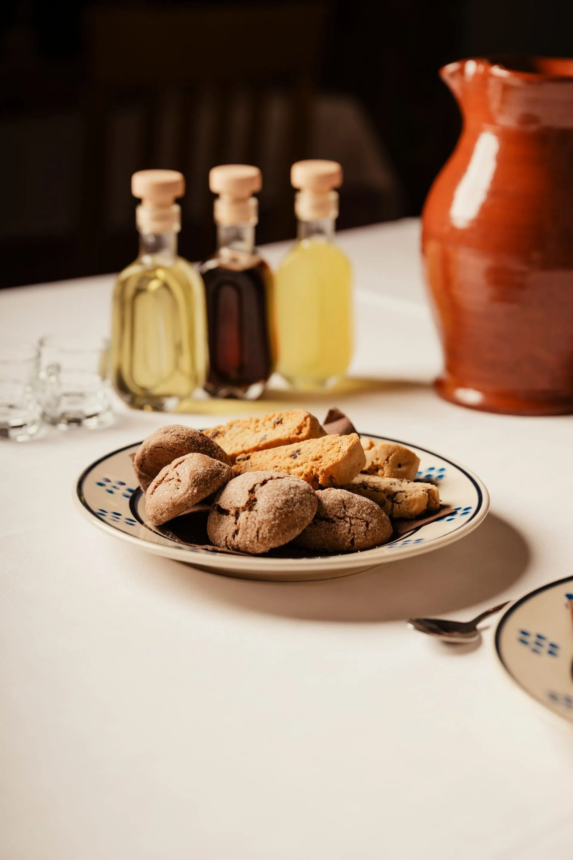 Plate of cookies on a table with small bottles and a red pitcher in the background