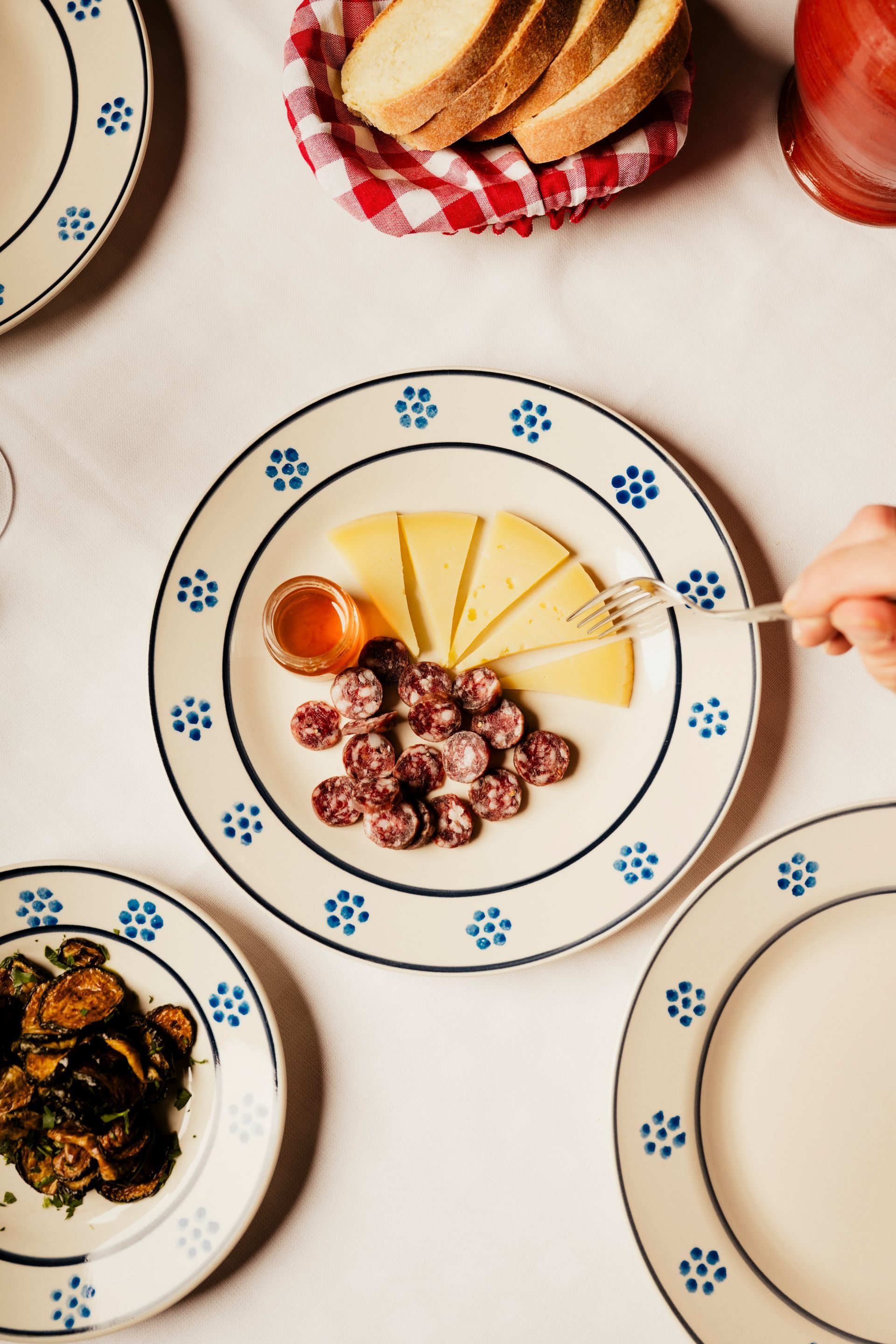 Plated dessert with sliced fruit and chocolate pieces on a patterned table, with bread and jam nearby