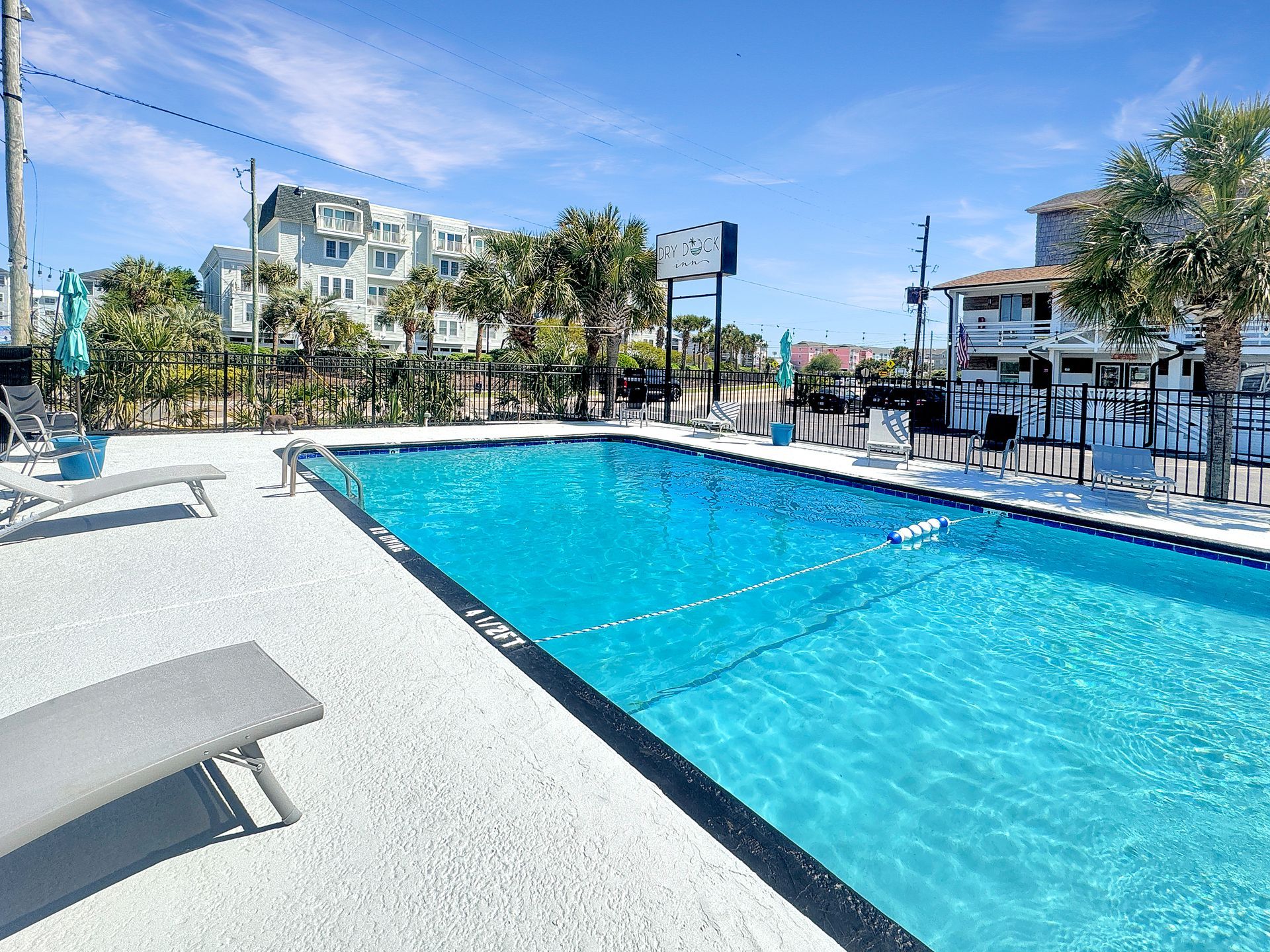 Swimming pool with blue water, concrete deck, and lounge chairs under a clear sky.