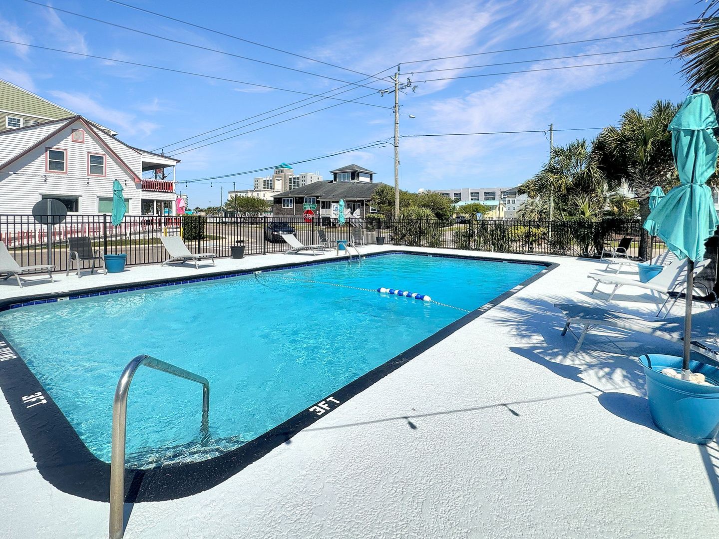 Pool with turquoise water, lounge chairs, and buildings under a sunny sky.