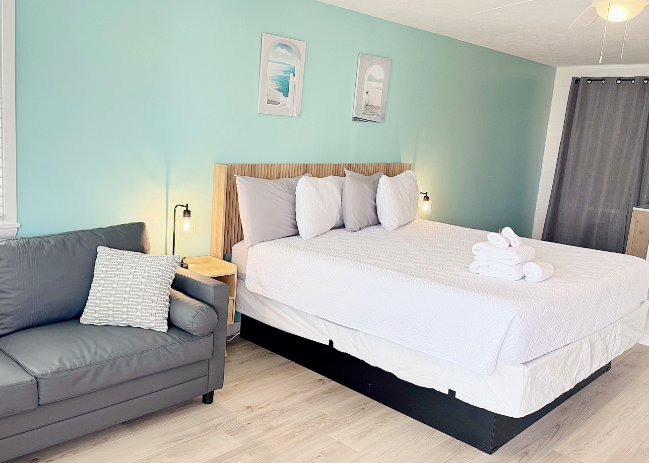 Bedroom with bed, sofa, and light blue wall. Includes artwork and a lamp.