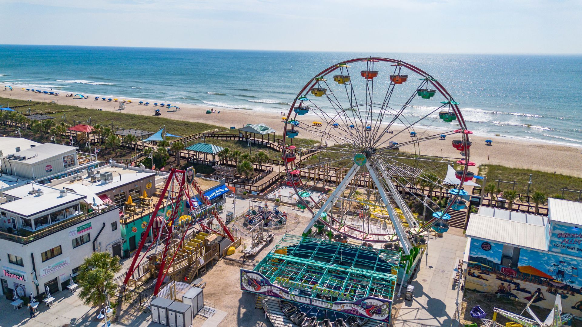 Ferris wheel and amusement park rides on a beach; ocean in the background.
