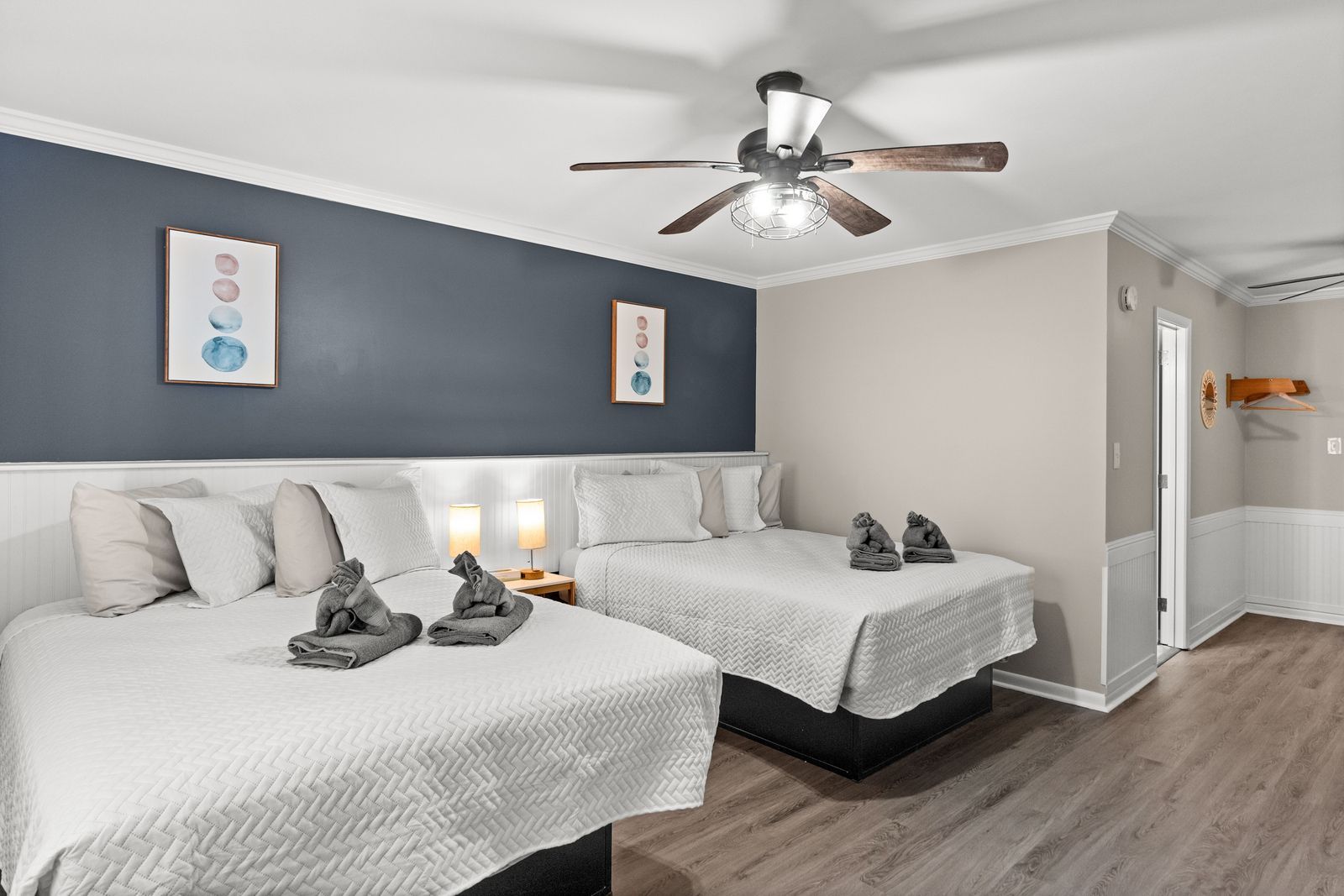 Bedroom with two beds, gray and white color scheme, artwork on the wall, ceiling fan, open door.