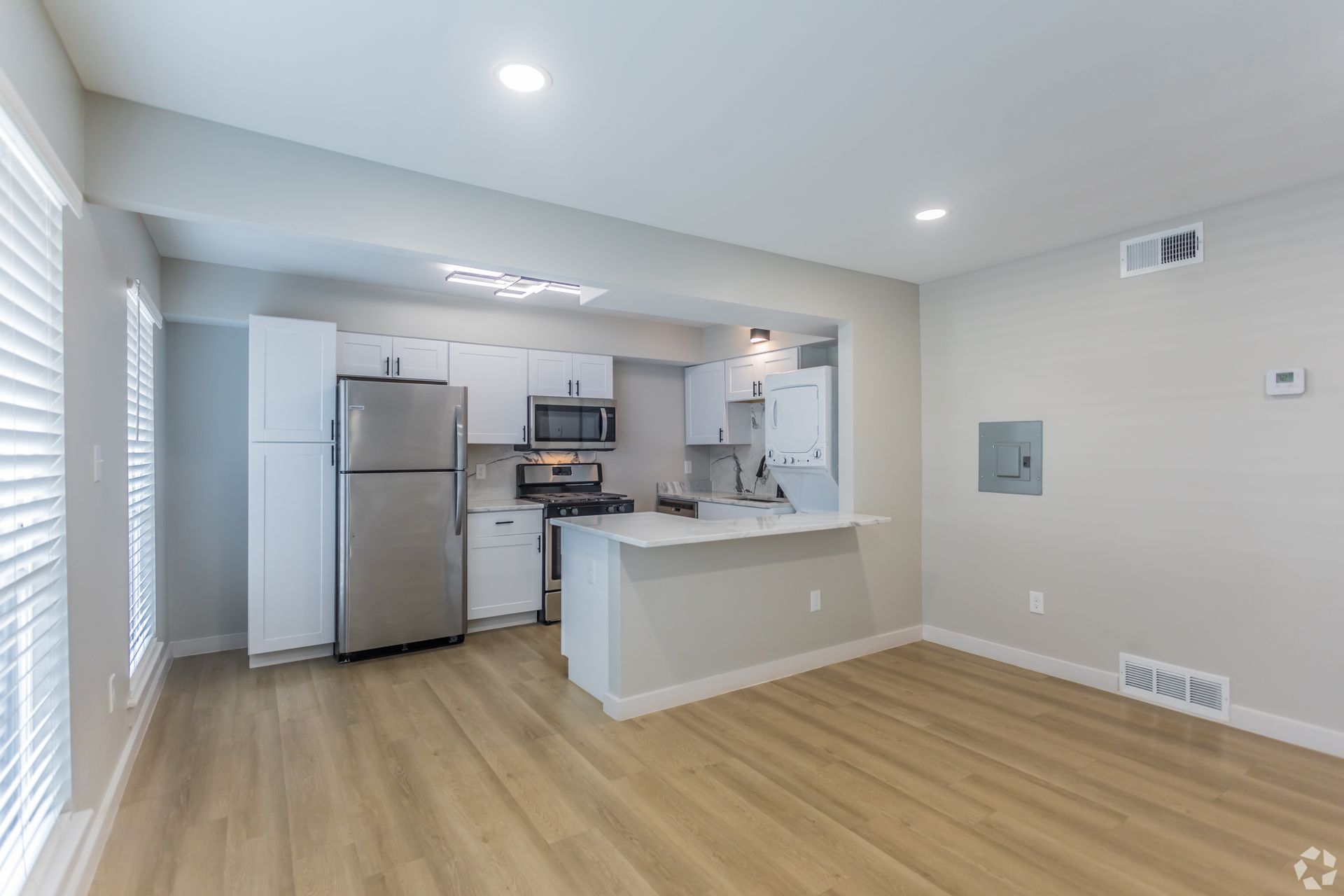 A modern, open-concept kitchen with white cabinets, stainless steel appliances, and wood-style flooring.