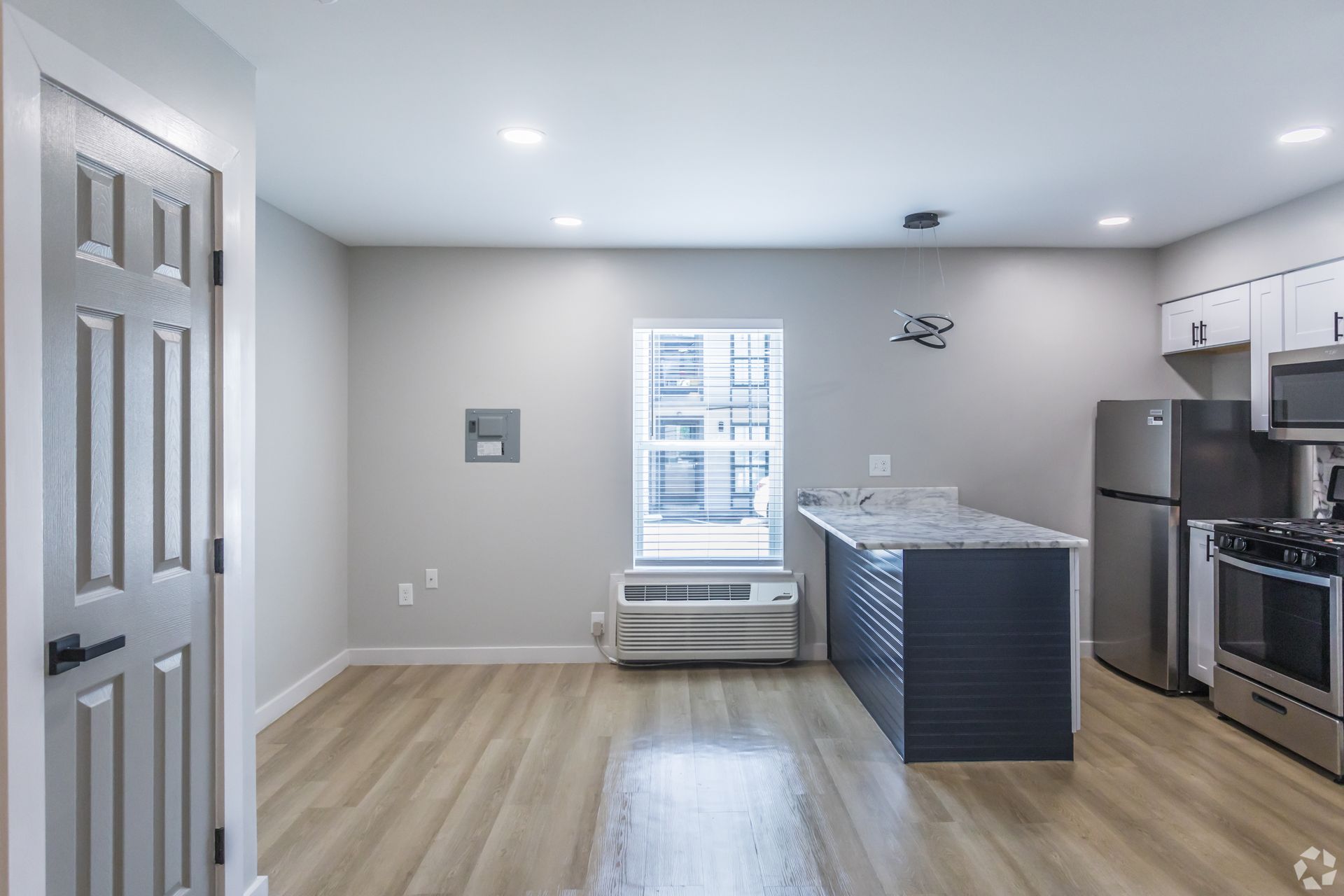 A modern apartment kitchen with light flooring, a blue-gray kitchen island, white cabinets, and stainless steel appliances.