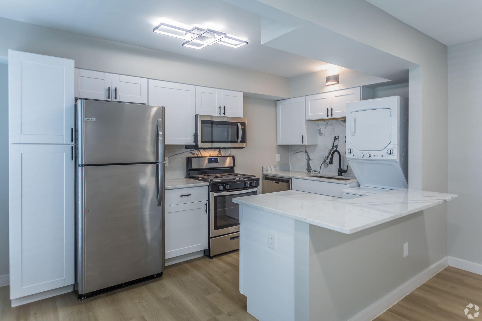 A modern kitchen with white cabinets, stainless steel appliances, and a marble-topped breakfast bar.