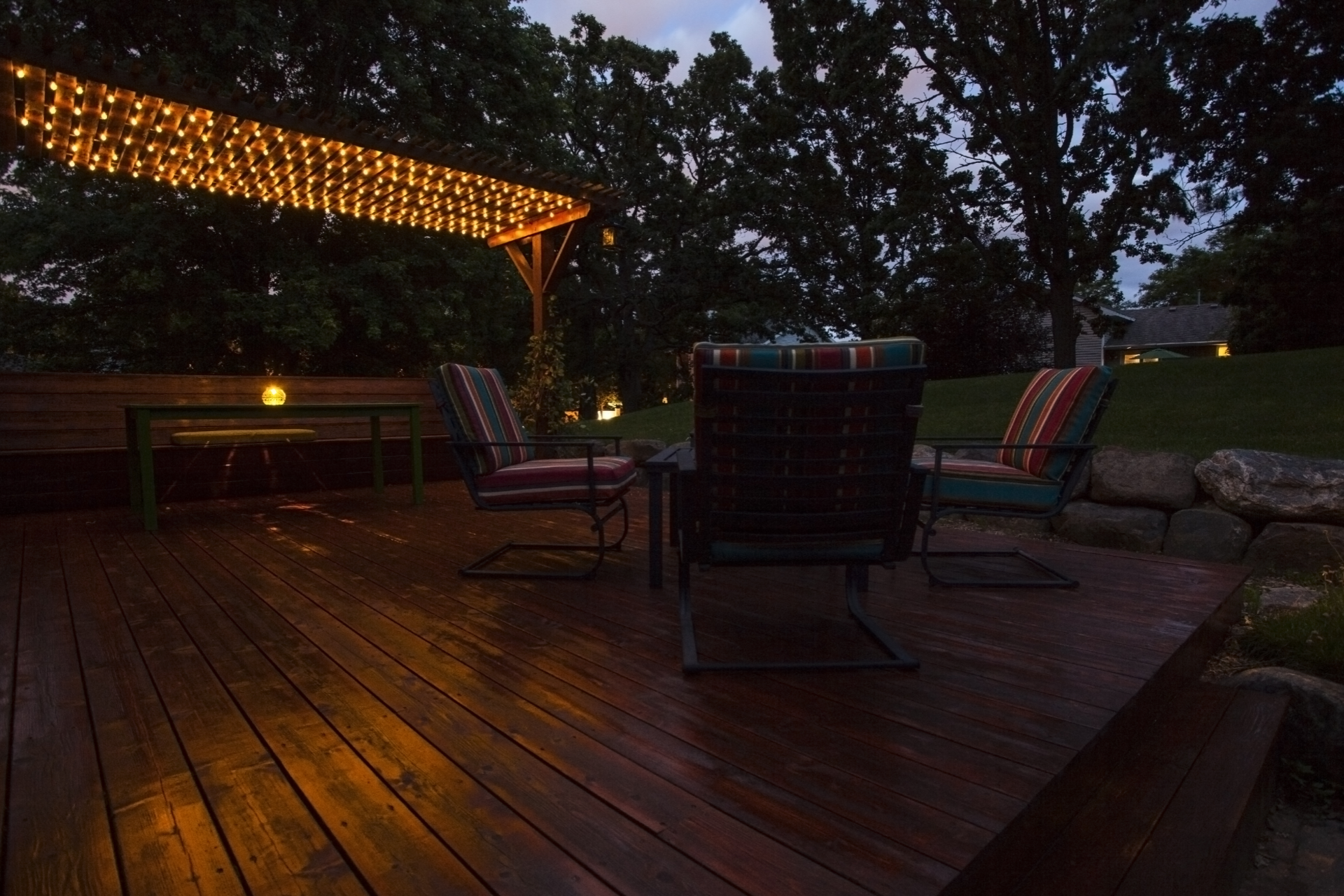 A photo of a deck built by Desert Dream Decks. The photo was taken at night to show off the lights hanging from the built-in pergola on the deck.