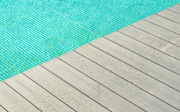 An up-close photo of a deck right next to a pool. The pool deck is gray. 