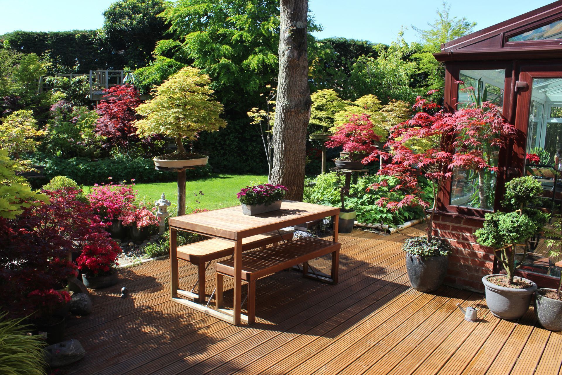 Wooden deck with furniture, vibrant garden, and conservatory.
