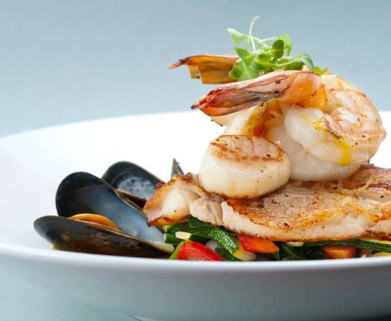 Un piatto bianco con gamberi, capesante, cozze e verdure