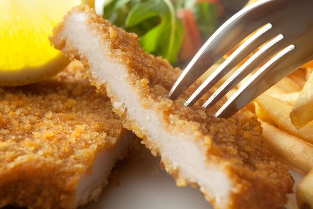 Una persona sta tagliando un pezzo di pollo fritto con una forchetta.