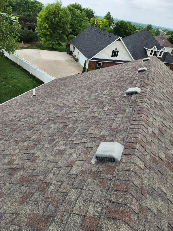 A roof with a lot of vents on it and a house in the background.