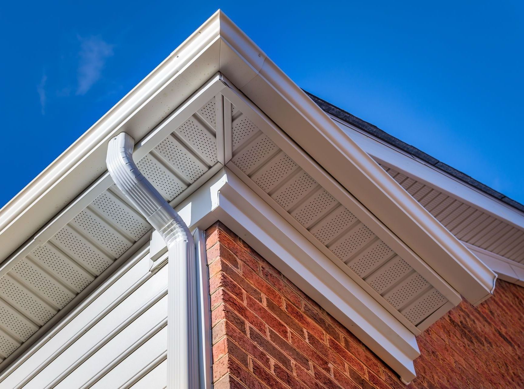 The corner of a brick house with white siding and gutters