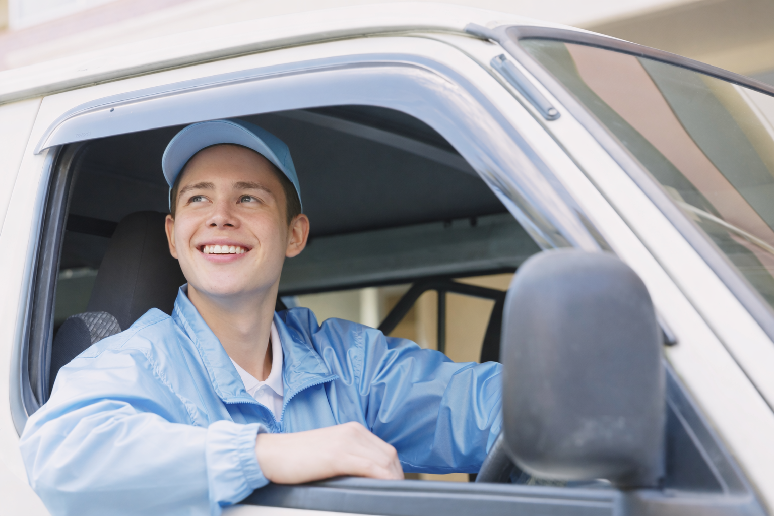 Smiling person in blue work uniform driving a vehicle, looking upwards.