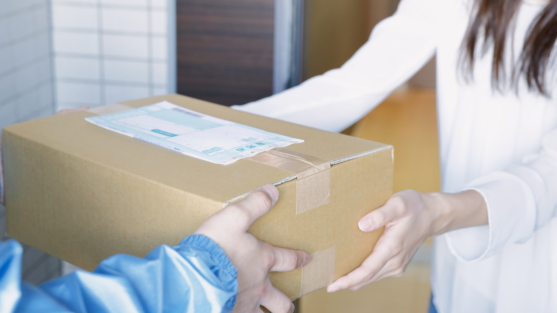Delivery person handing a cardboard box to a person outside a building.