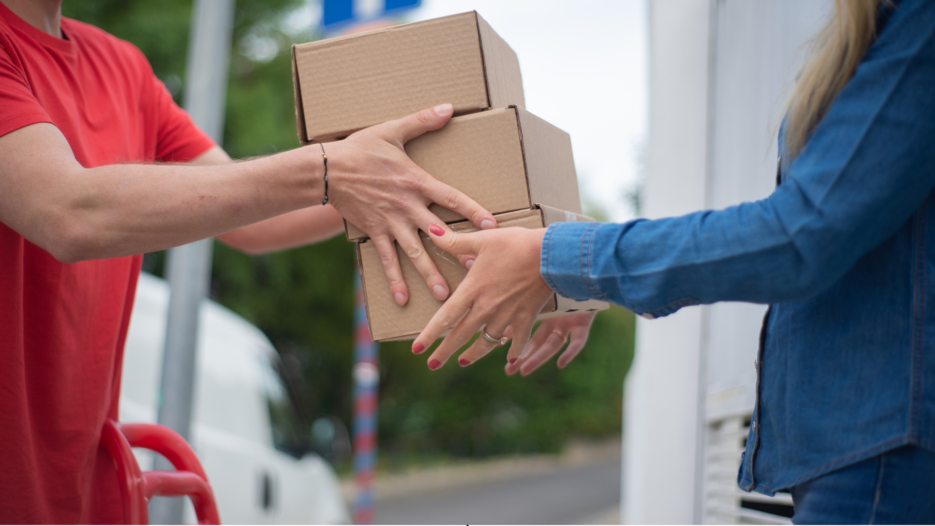 A delivery man is handing a stack of boxes to a woman.