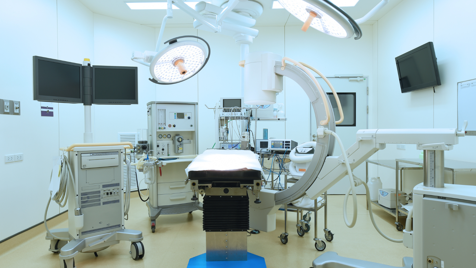 An empty operating room with a bed , monitors , and other medical equipment.