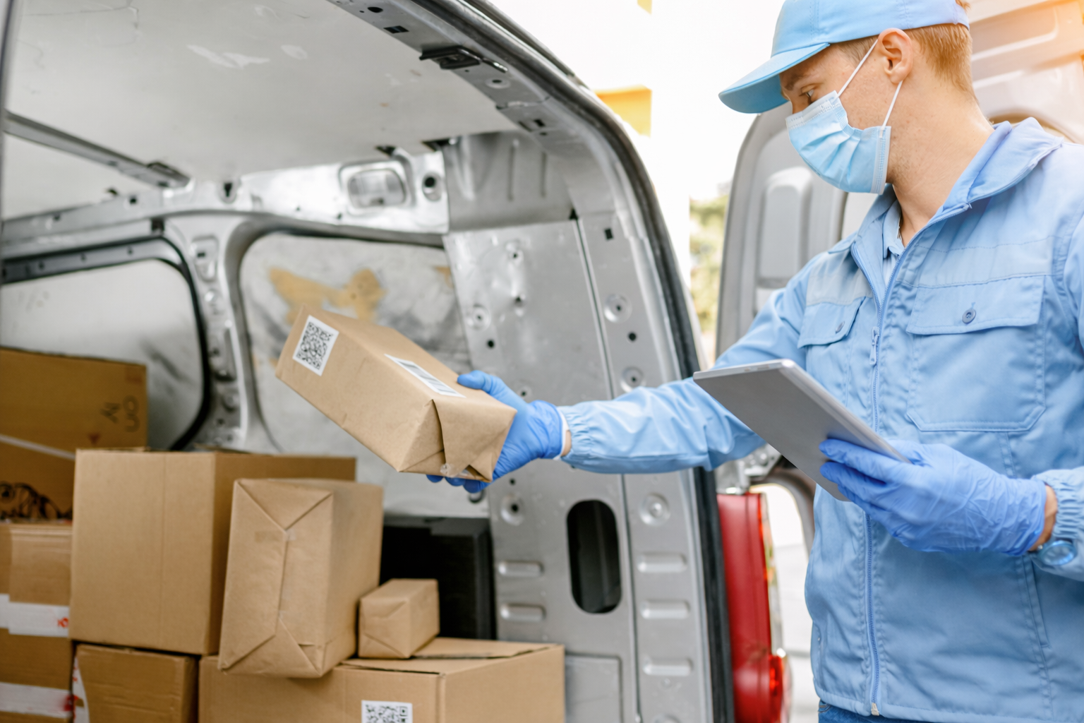 Delivery person in blue uniform and mask loading package into delivery van.