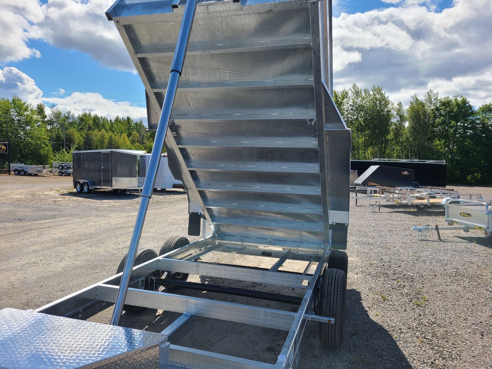 Une remorque à benne basculante avec des escaliers menant à elle est garée dans un terrain en gravier.
