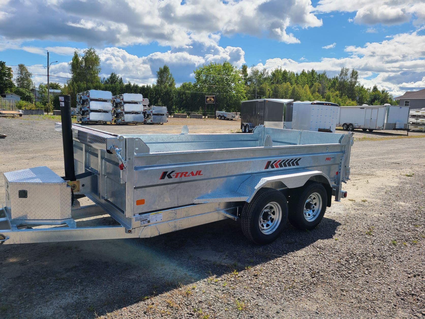 Une remorque à benne basculante est garée sur un terrain en gravier.