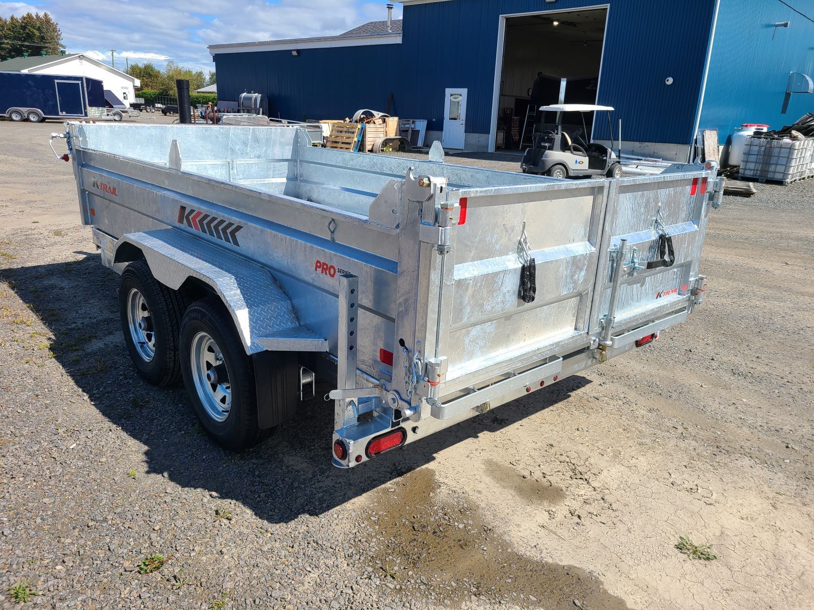 Une remorque à benne basculante est garée devant un bâtiment bleu.