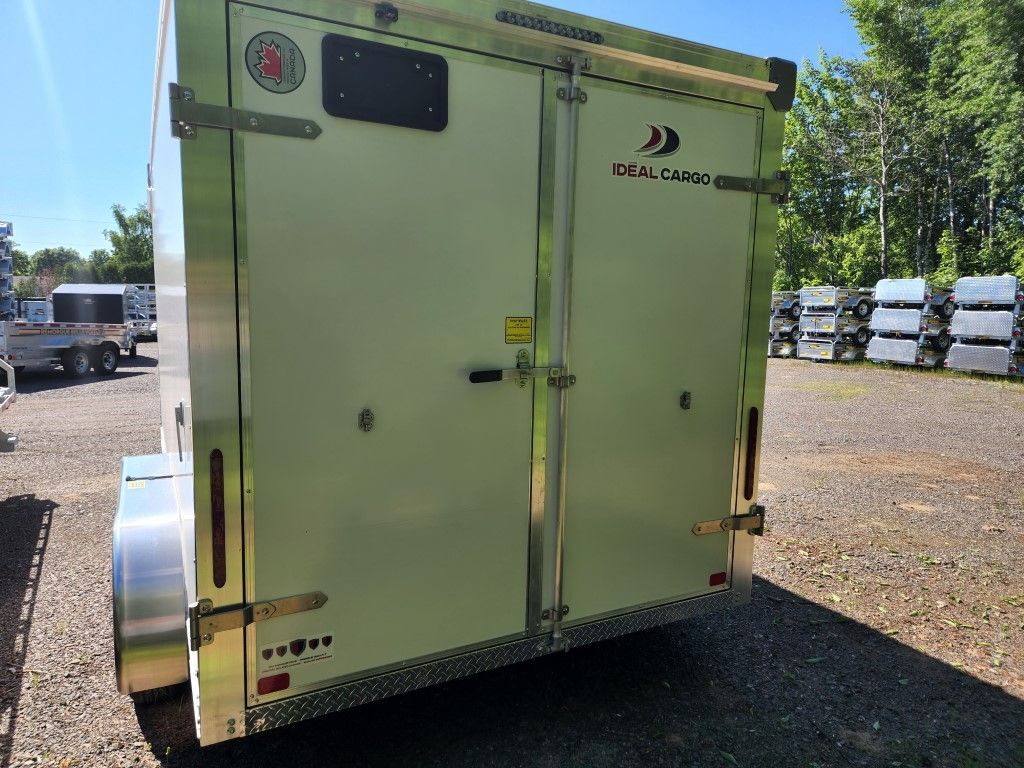 Vue arrière d'une remorque fermée argentée à double porte. La remorque est stationnée à l'extérieur sur du gravier.