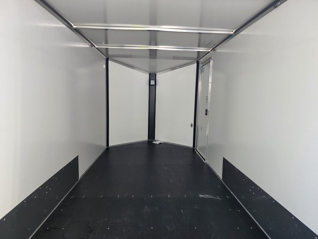 Intérieur d'une remorque fermée et vide, sol noir, murs blancs et une porte au fond.
