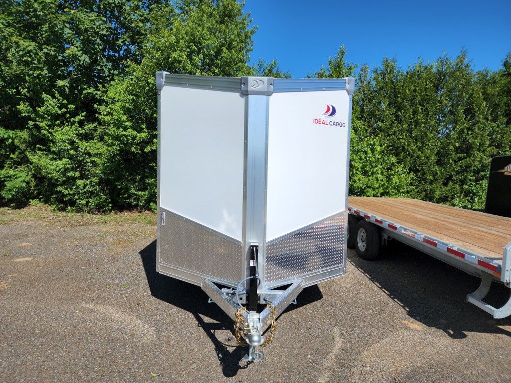 Remorque blanche fermée avec des accents en aluminium, stationnée sur le trottoir.