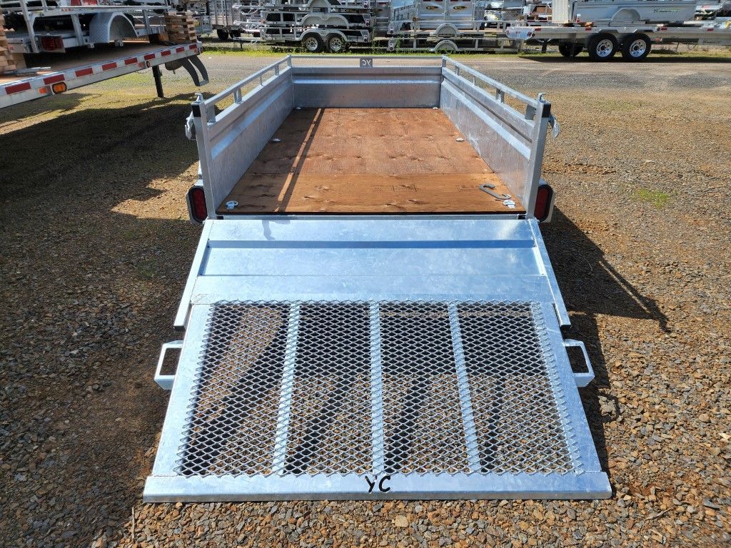 Une remorque avec une rampe est posée sur un terrain en gravier.