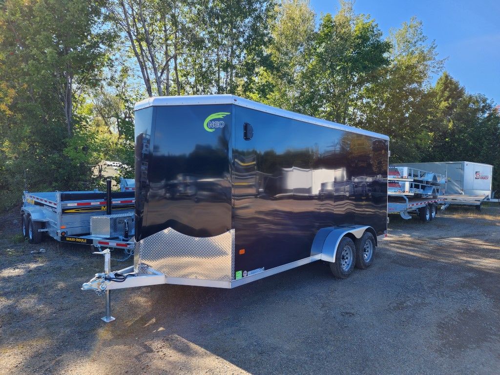 Remorque cargo fermée noire garée sur du gravier, avec d'autres remorques en arrière-plan.