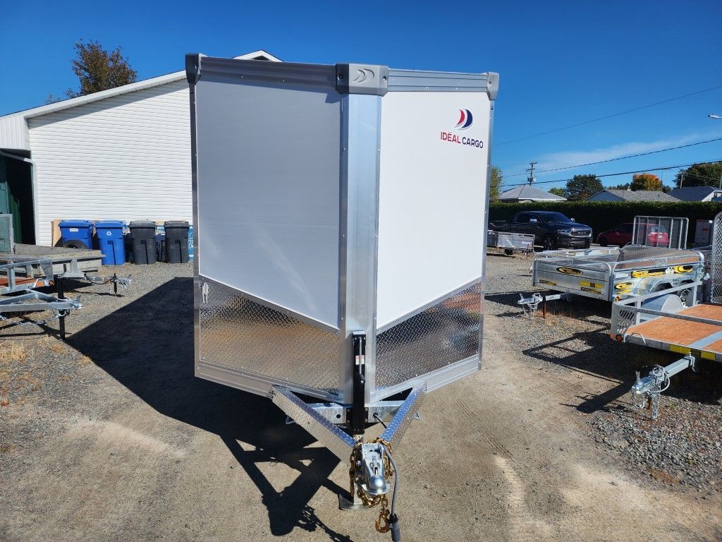 Remorque cargo argentée et blanche avec façade en tôle diamantée, garée à l'extérieur par une journée ensoleillée.