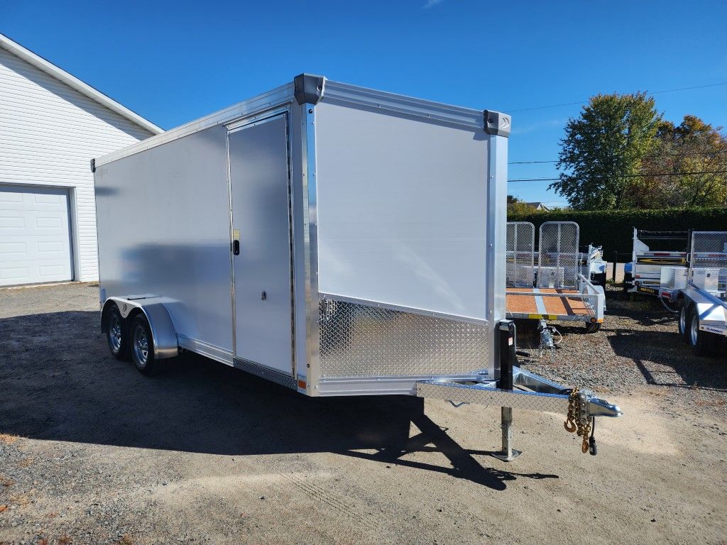 Remorque cargo fermée en aluminium avec une face avant en tôle diamantée, devant un bâtiment.