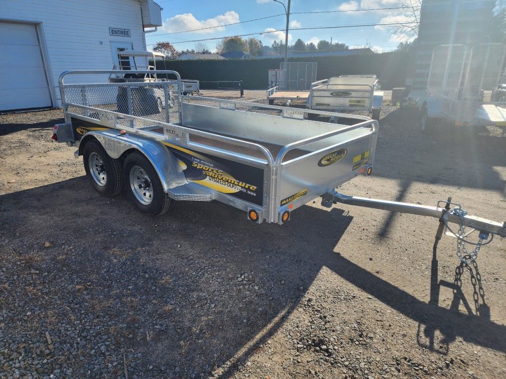 Une remorque est garée sur un terrain en gravier devant un garage.