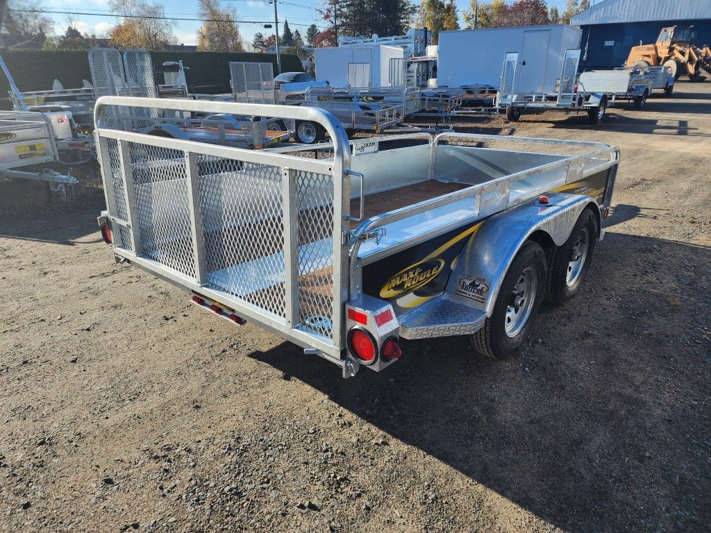 Une remorque est garée sur un terrain en terre devant un bâtiment.