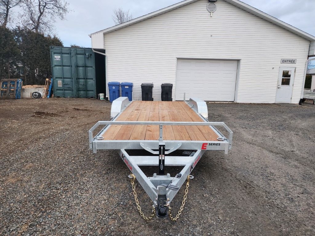 Une remorque à plateau est garée devant un garage.