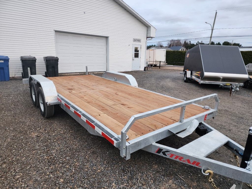 Une remorque avec un pont en bois est garée devant un bâtiment.