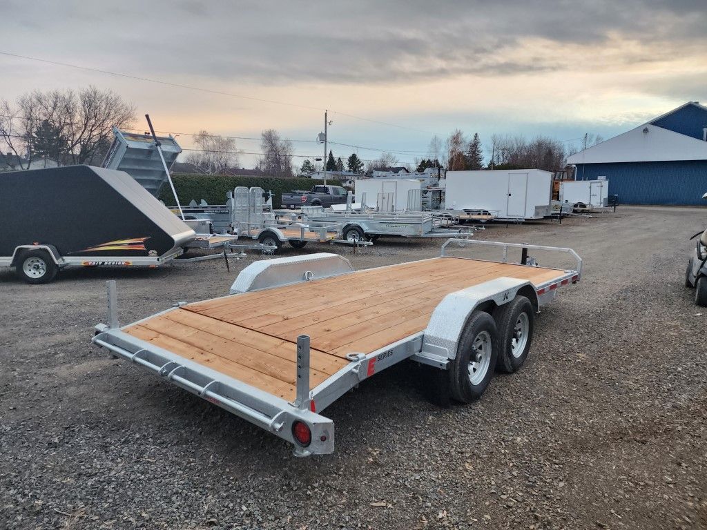 Une remorque avec une terrasse en bois est garée sur un terrain en gravier.