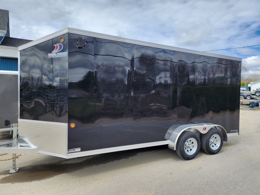 Remorque fermée noire avec garniture argentée et deux roues, stationnée à l'extérieur.