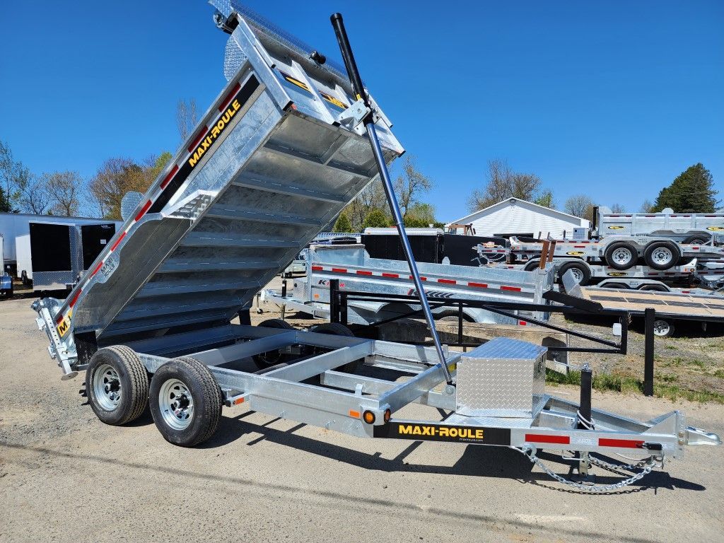 Remorque à benne basculante argentée soulevée, par une journée ensoleillée. Remorque à deux essieux, dans un parking avec d'autres remorques.