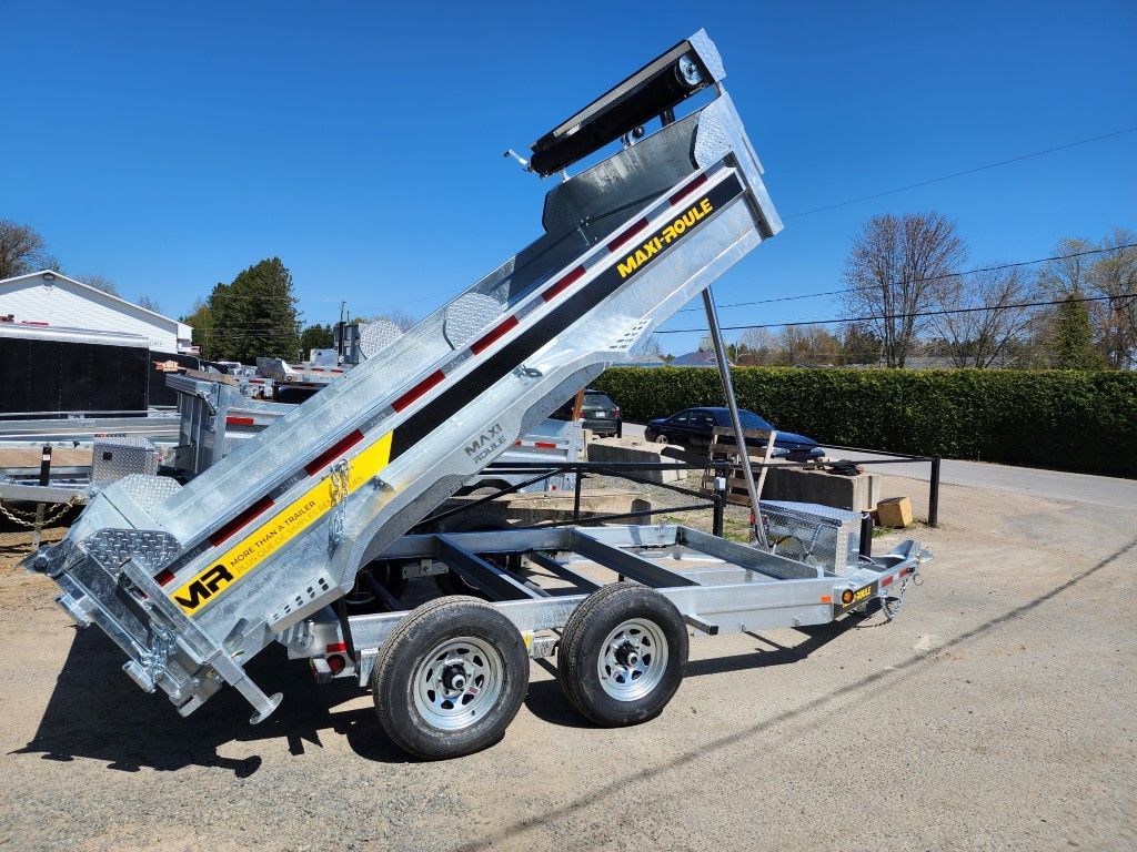 Remorque à benne basculante argentée à roues jumelées et plateau incliné, garée sur du béton. Journée ensoleillée.