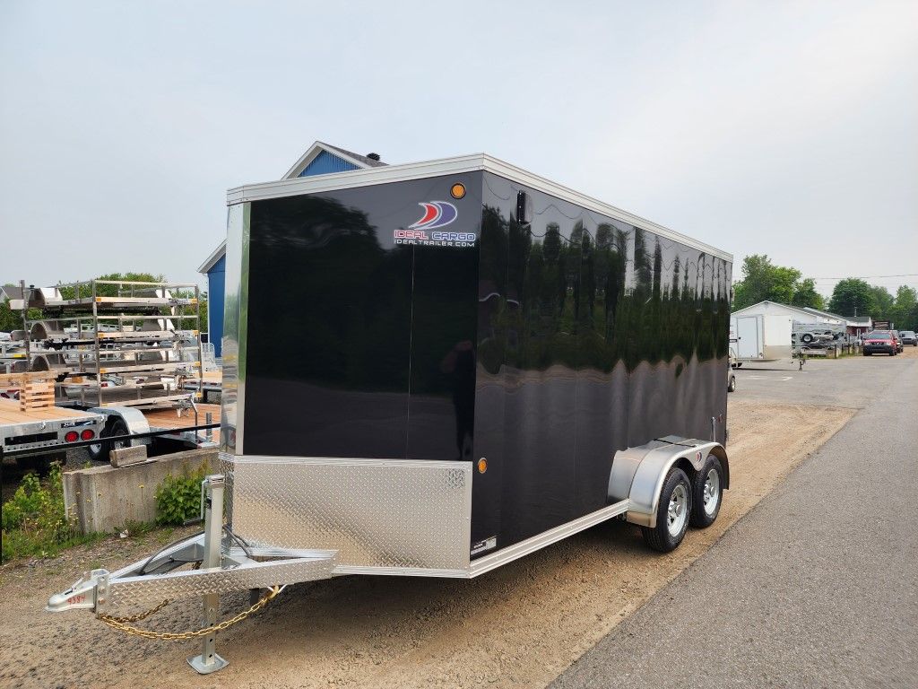 Remorque cargo fermée noire sur le trottoir, à l'extérieur, avec un bâtiment bleu en arrière-plan.