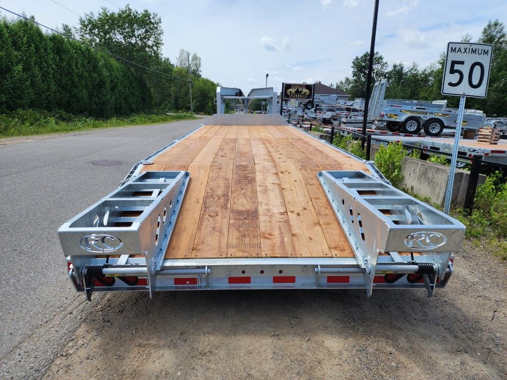 Remorque à plateau stationnée sur une route asphaltée, avec un panneau de limitation de vitesse visible.