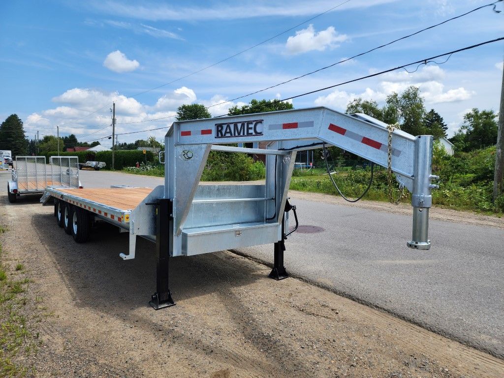 Remorque à plateau argentée sur une route, ciel bleu, logo RAMEC et pieds de support noirs.