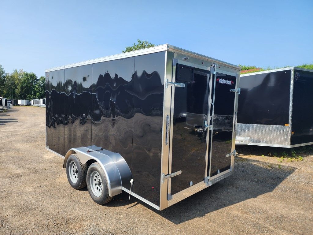 Une remorque noire est garée dans un champ de terre.