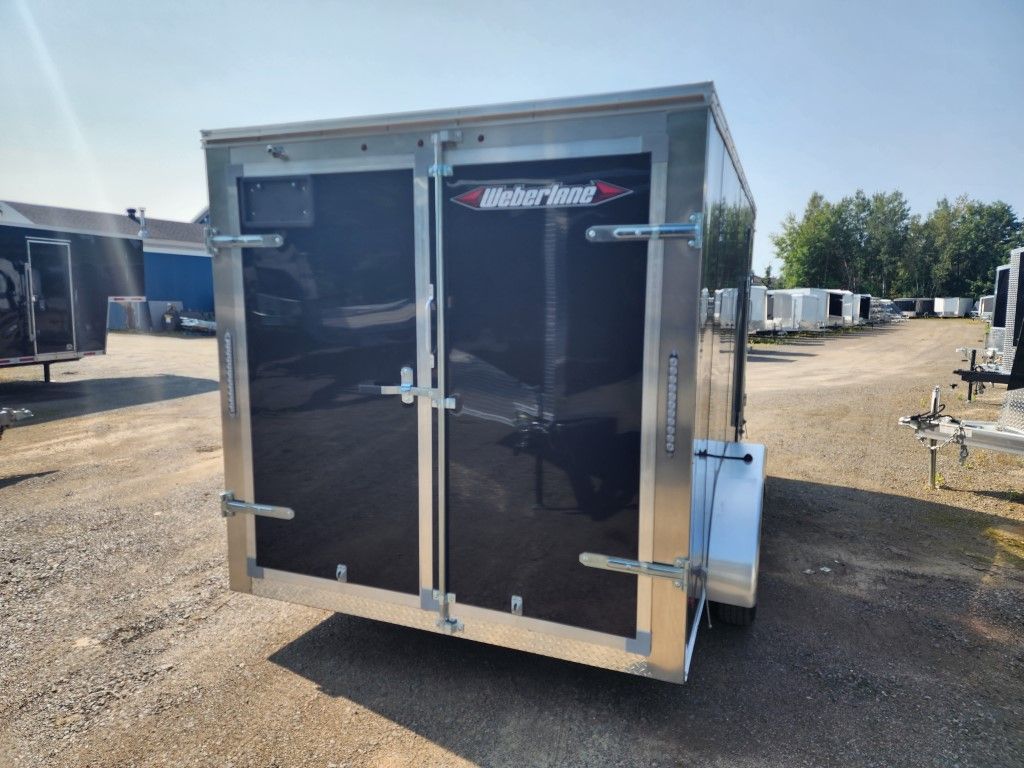 Une remorque noire et argentée est garée sur un terrain en gravier.