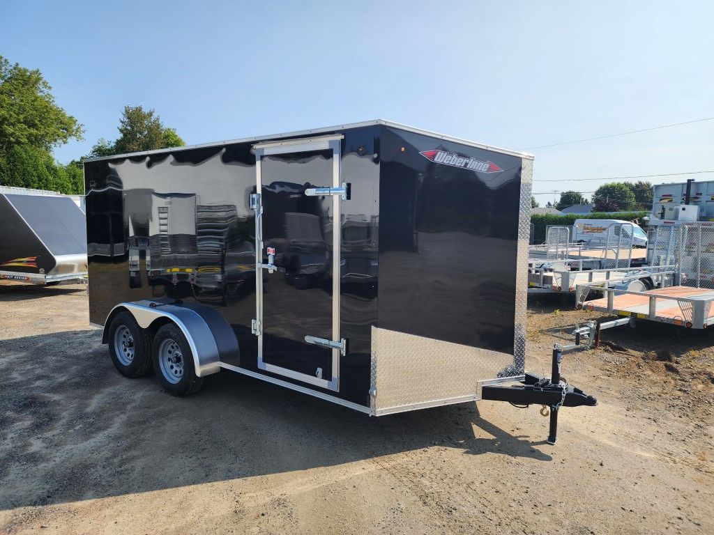 Une remorque noire et argentée est garée sur un terrain en terre.